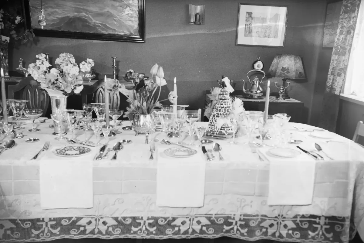 Svart-hvitt-foto av et dekket bryllupsbord med blomster, lys, krystallglass og kransekake