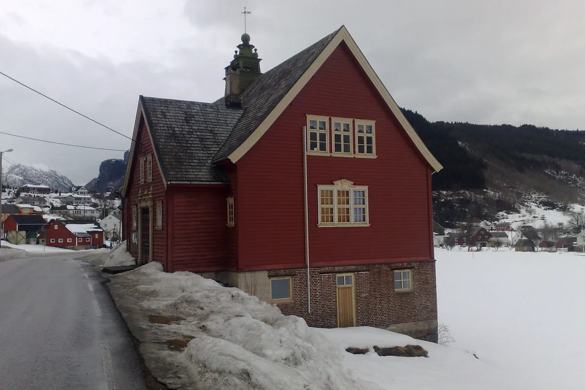 Rødt ungdomshus med tårn på taket, ved en vei med snø langs kanten