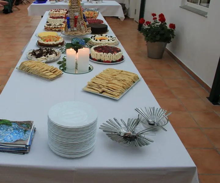 Langt kakebord med kransekake, bløtkaker, lys og stabler av asjetter
