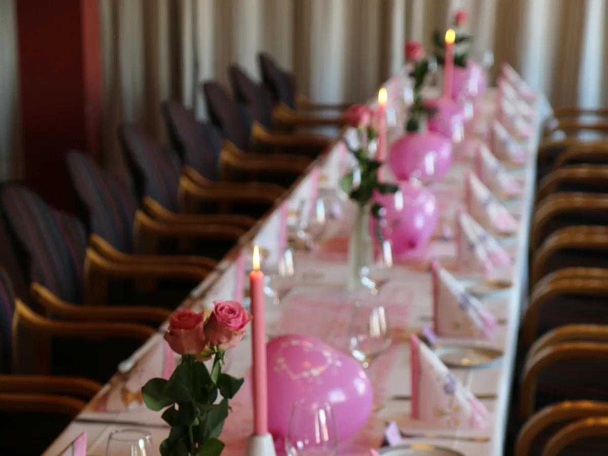 Langbord med hvit duk, rosa ballonger, roser og levende lys, klart til fest